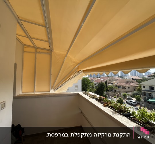 סוכך צהוב נפרש מעל מרפסת עם צמחייה
